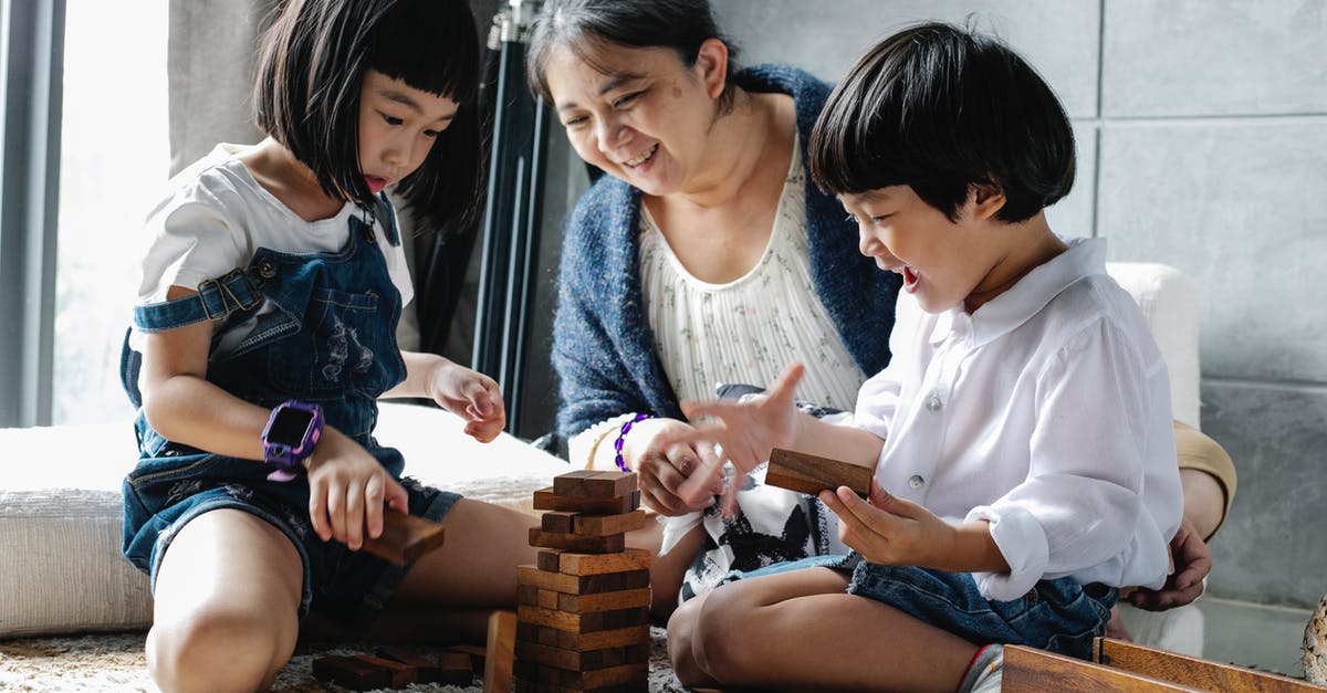 Draught of Living Death/Astronomy Tower Secret Room - Happy grandmother sitting on floor with Asian boy and girl while playing with wooden blocks and building tower in living room near window