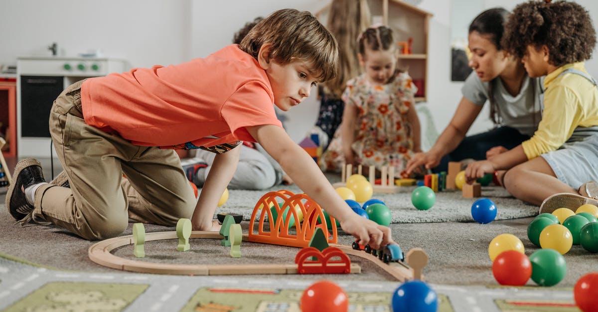 Education on the island [duplicate] - Boy in Orange Shirt Playing Train Toy on the Floor