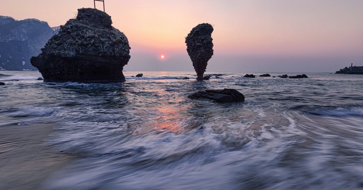 endless legend no watchtowers - Long exposure of small vibrant Sun in light blue pink sky over mountain range and cliffs next to coast of endless wavy ocean in evening at dawn