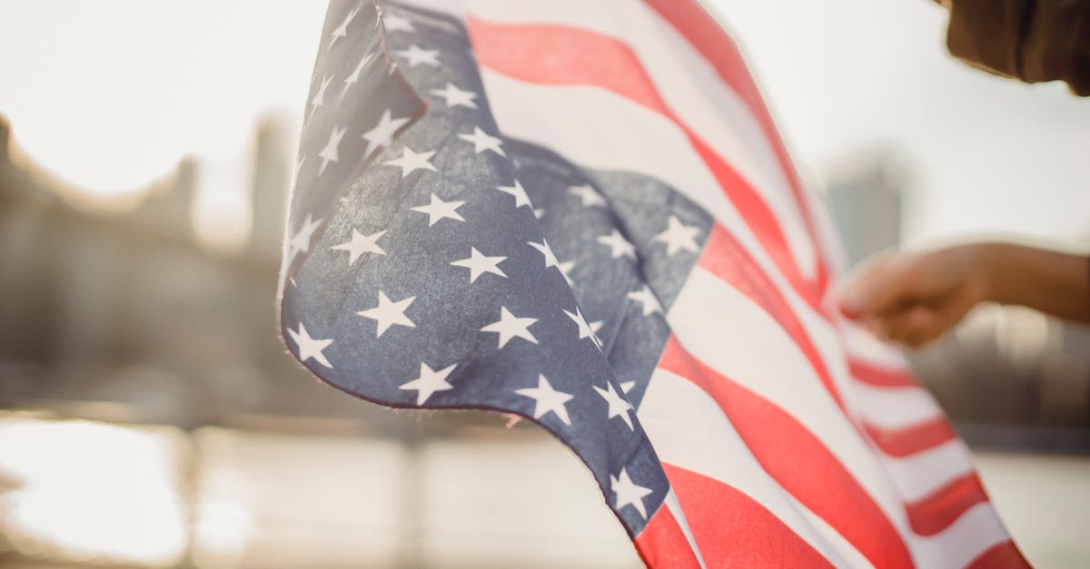 Enforcing Culture on Personal Union - From below of crop person holding national flag of United States of America waving in wind on street against city river