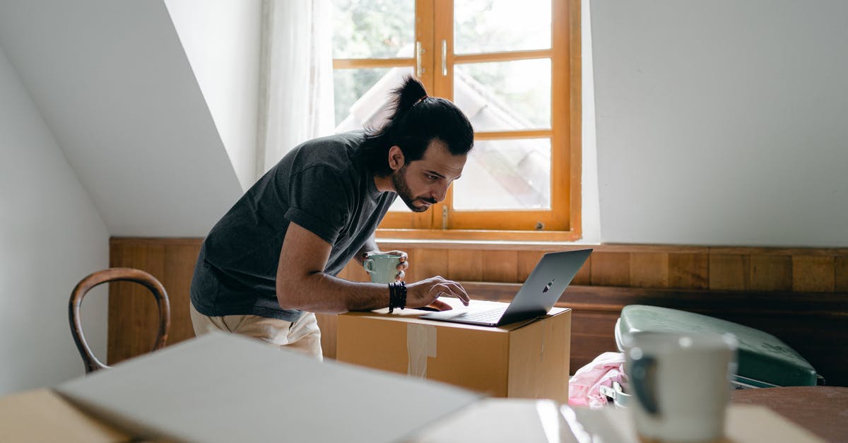 Enigma data pack in the Royal Hotel's ballroom is inaccessible - Side view of focused bearded male in casual outfit with cup of hot drink browsing laptop while packing stuff into carton boxes