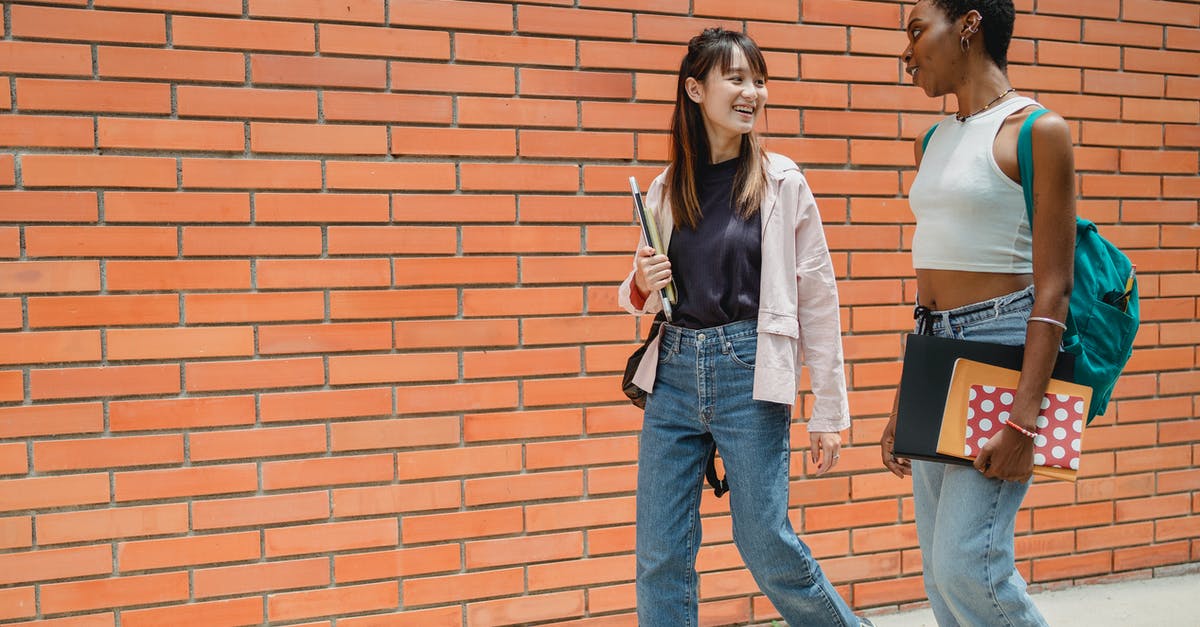 Exp. Share and Pokérus in second generation (GSC) - Positive African American female student with notebooks and backpack communicating with female friend wearing jeans while walking together near brick wall of university