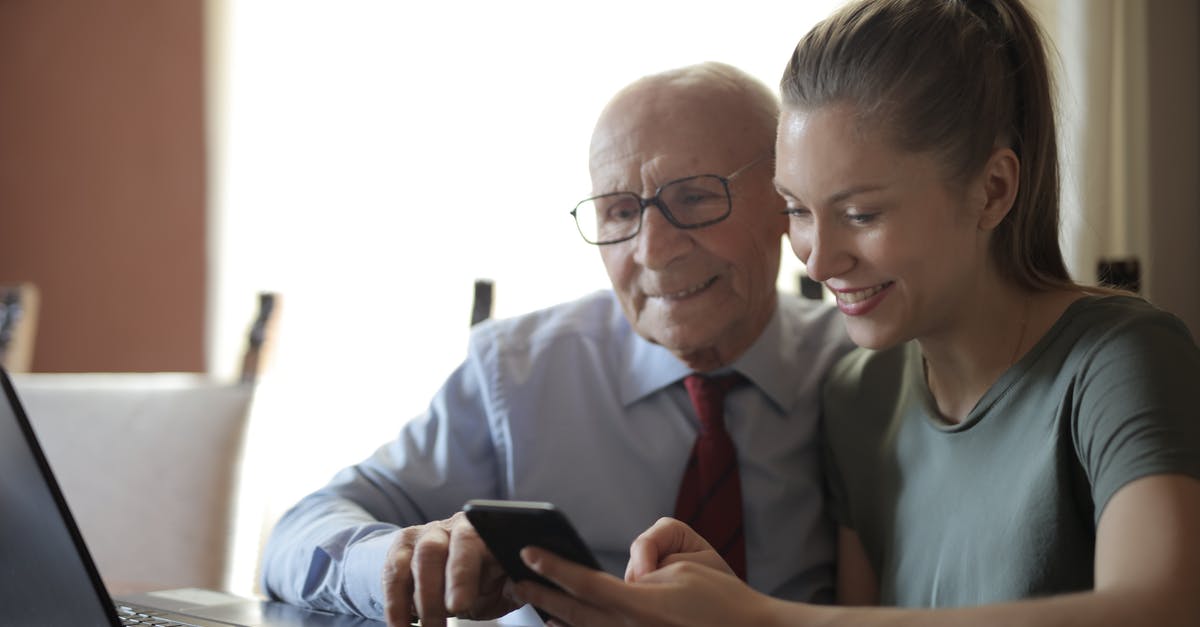 Exp. Share and Pokérus in second generation (GSC) - Positive senior man in formal shirt and eyeglasses and smiling young granddaughter sharing mobile phone while sitting near laptop at table