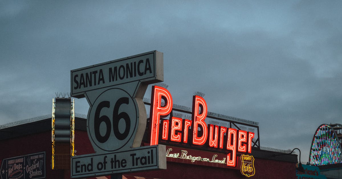 Finding the End city - Low angle of road sign with Route 66 End of the Trail inscription located near fast food restaurant against cloudy evening sky on Santa Monica Beach