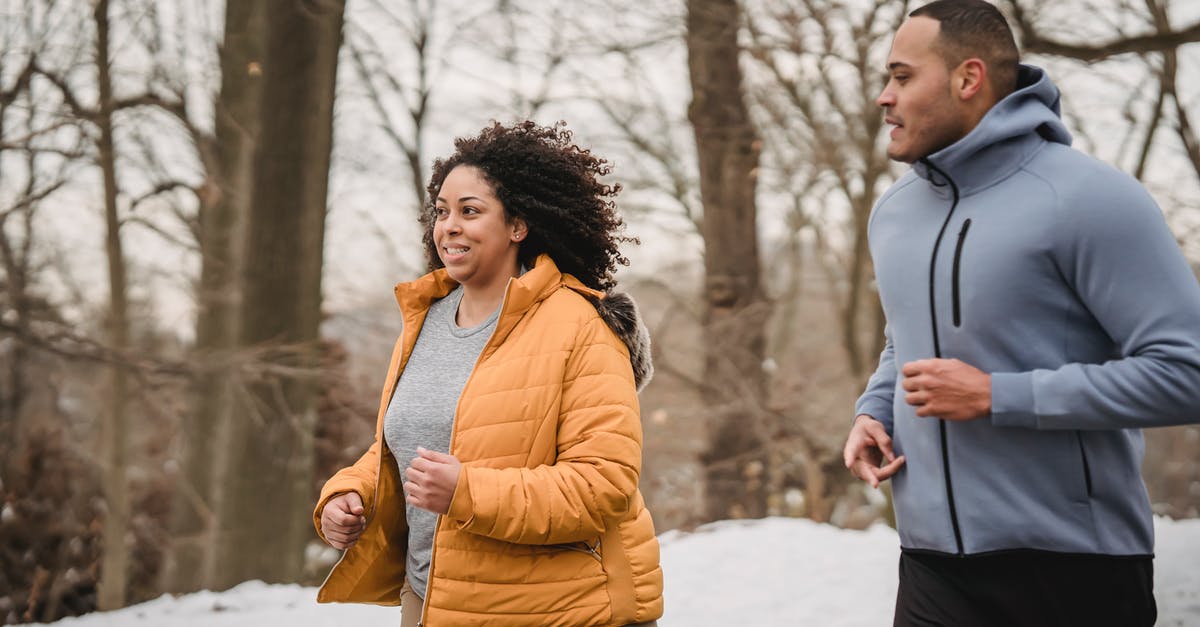 Help me run the numbers on a perfect IV ditto - Cheerful plus size African American female in warm outerwear running with black personal trainer in snowy park during training in winter time