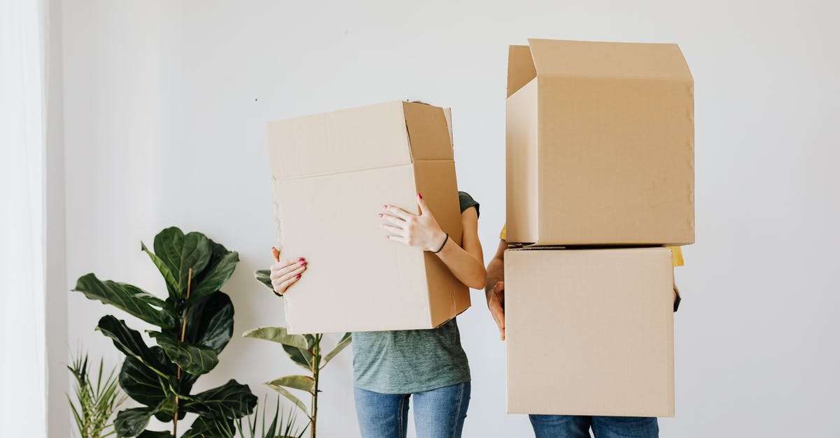 How can I carry more stuff? - Unrecognizable couple wearing jeans standing carrying stacked carton boxes out of apartment during renovation on daytime