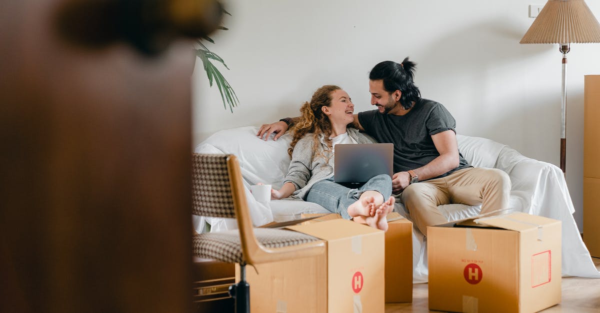 How can I move population to other colonised systems? - Cheerful couple in casual clothes sitting on comfortable sofa with laptop and looking at each other while moving to new apartment