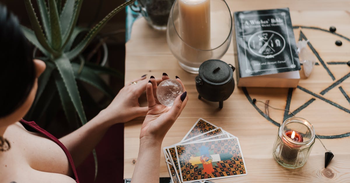 How can I separate differents enchantments from a book - From above of crop unrecognizable female soothsayer with magic ball near tarot cards and candles during divination process in house