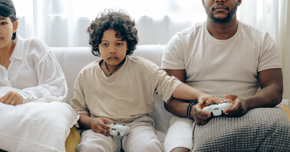 How can I show enemy health using console? - Concentrated child showing usage of gamepad to father while playing on game console and resting on sofa together with family