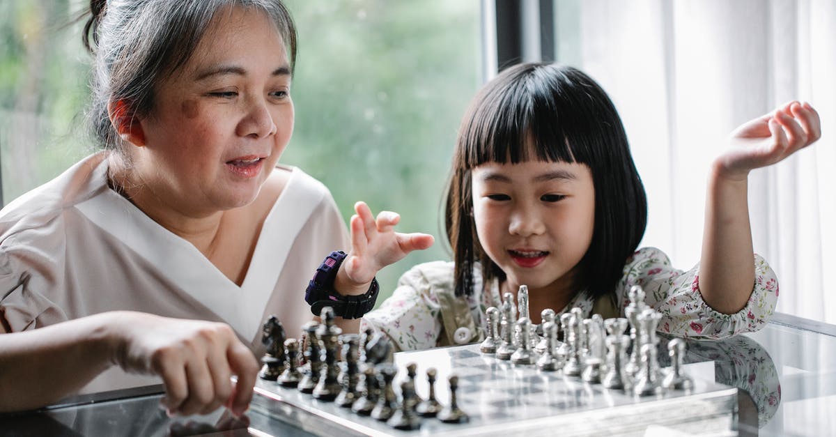 How can I teach my Pokémon a moved it skipped? - Positive Asian grandmother or nanny in casual wear teaching smiling adorable girl to play chess in light room