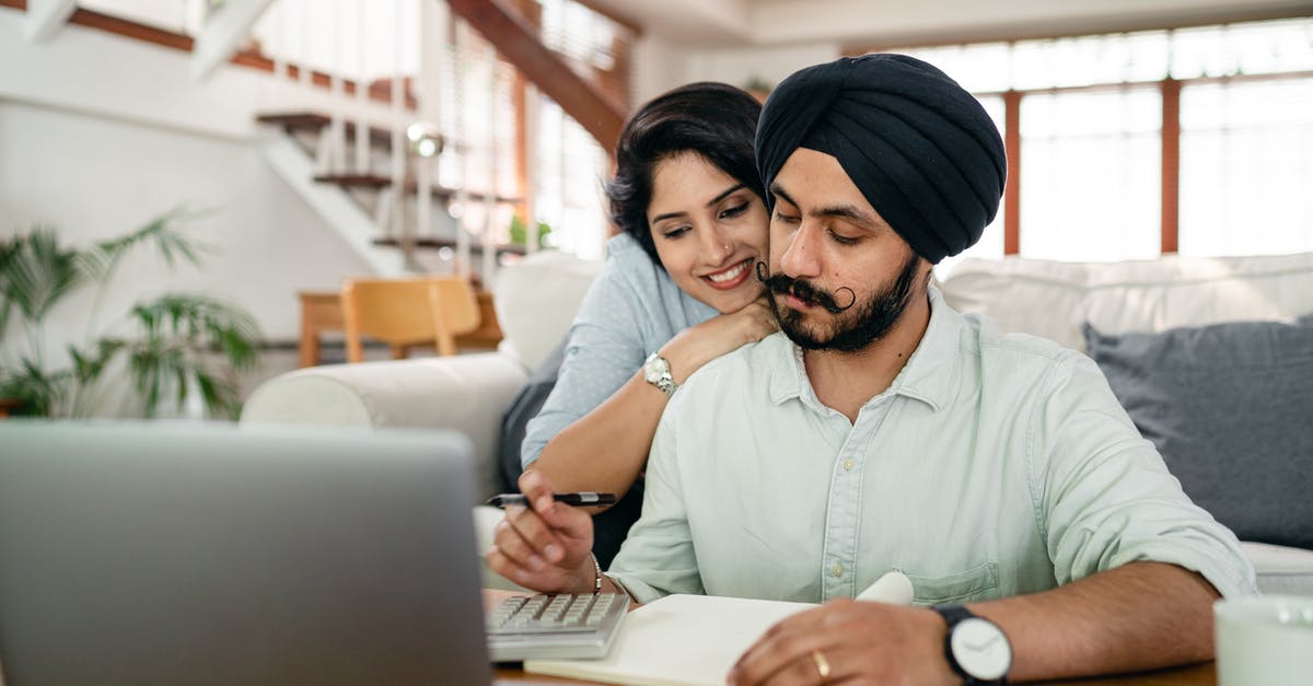 How do activities with my spouse work? - Cheerful young Indian woman cuddling and supporting serious husband working at home with laptop and counting on calculator