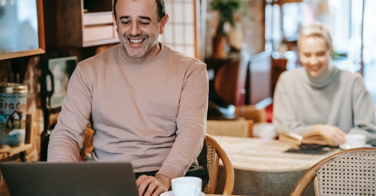 How do activities with my spouse work? - Cheerful middle aged ethnic man smiling while working remotely on laptop near positive wife reading book and drinking coffee