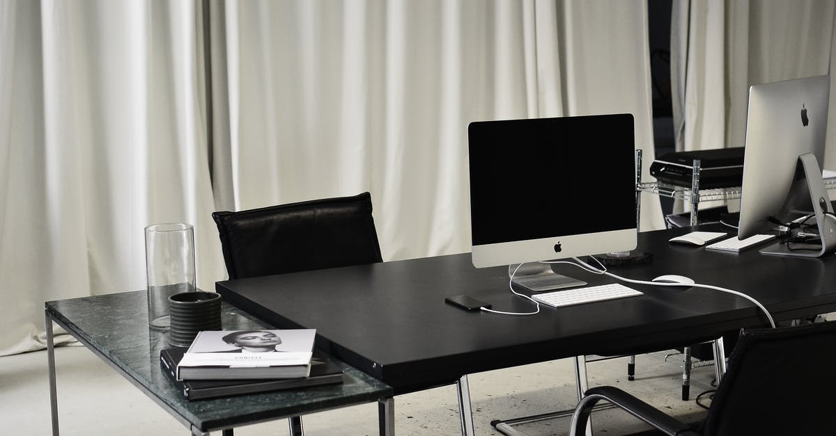 How do estus charges work? - Black and white of workspace of office with computers placed on table with wireless mouse and keyboard near smartphone