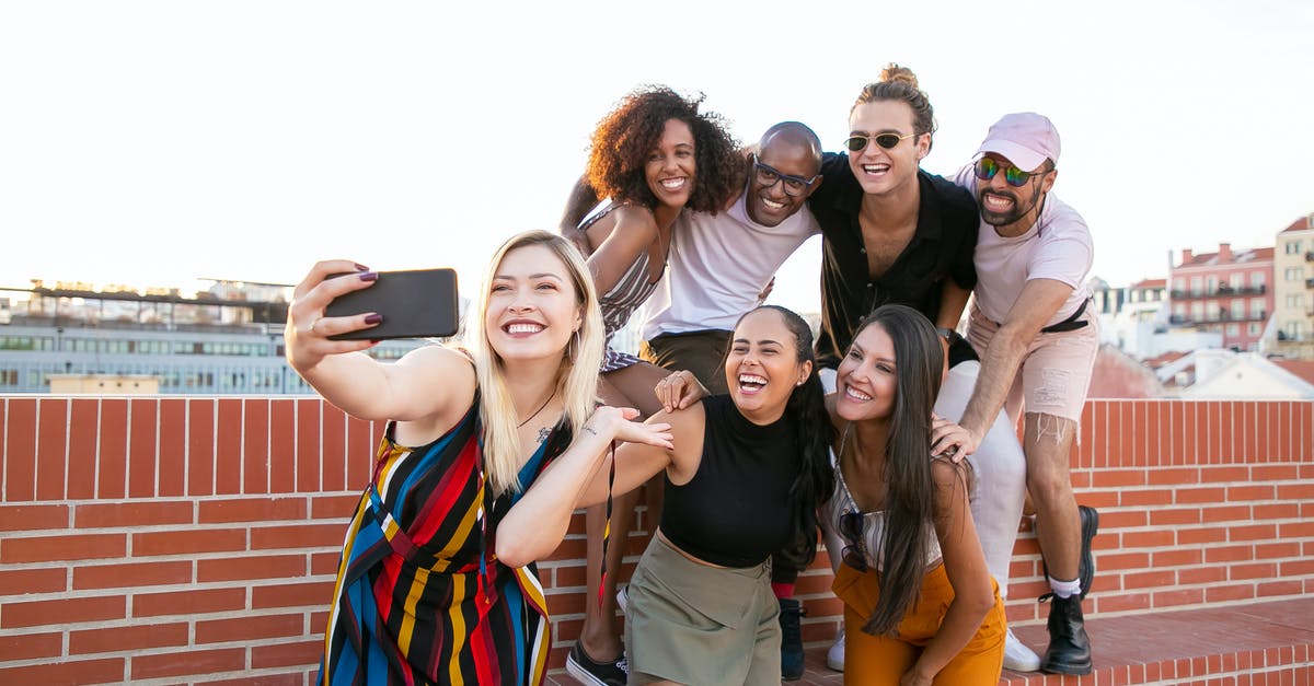 How do I capture a ship? - Group of cheerful young male and female multiracial friends laughing and taking selfie on smartphone while spending time together on terrace