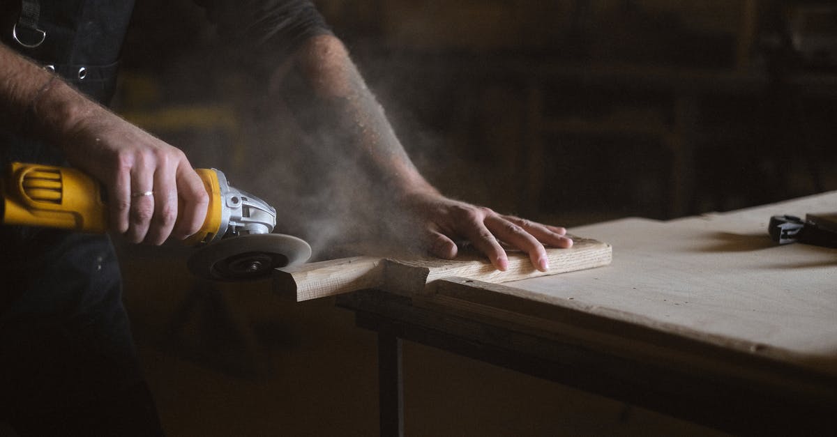 How do I efficiently grind skills? - Unrecognizable male master using electric angle grinder to polish lumber plank while standing at table in professional joinery during work