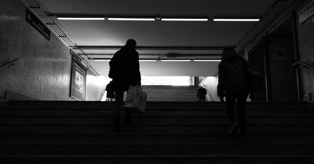 How do I go back to motherbase in MGS:TPP? - Back view black and white of anonymous passengers walking up staircase leaving subway station