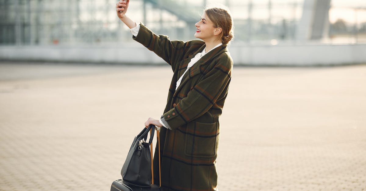 How do I make a city recover from a disastrous flood? - Stylish young woman with luggage taking selfie outside modern glass building