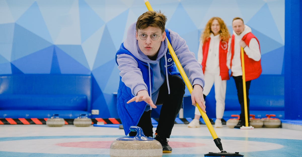 How do I move a rock? - Concentrate male in sportswear with broom in hand throwing granite curling stone sliding on ice sheet while playing game near team