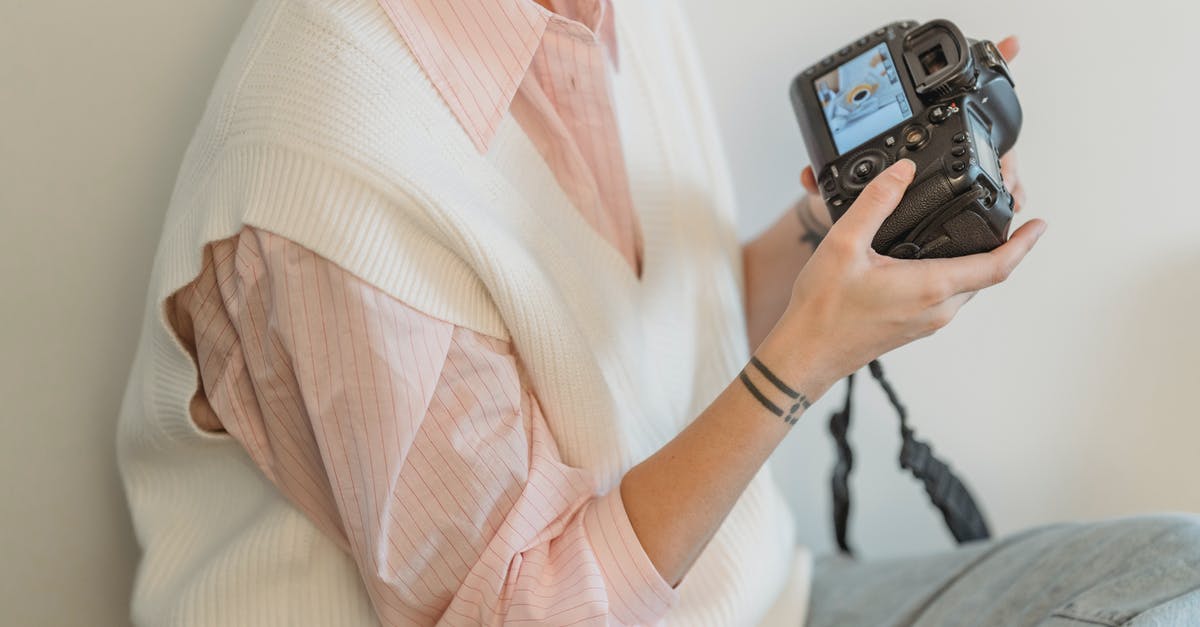 How do I take my badges out and look at them? - Crop anonymous female photographer wearing casual clothes looking through pictures in professional photo camera against white wall in light room