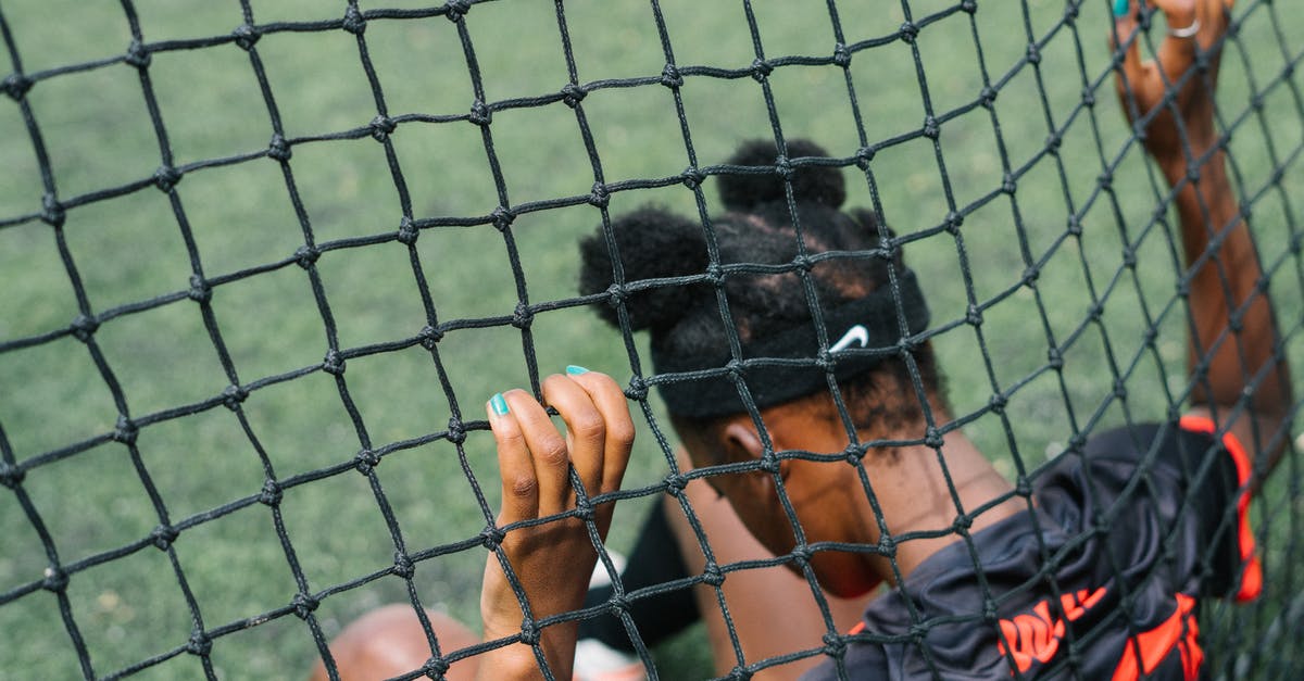 How do I trade Pokémon between two emulated generation 4 games? - Back view of African American teenage football player sitting on field ground and holding grid of gate while preparing to start play football match