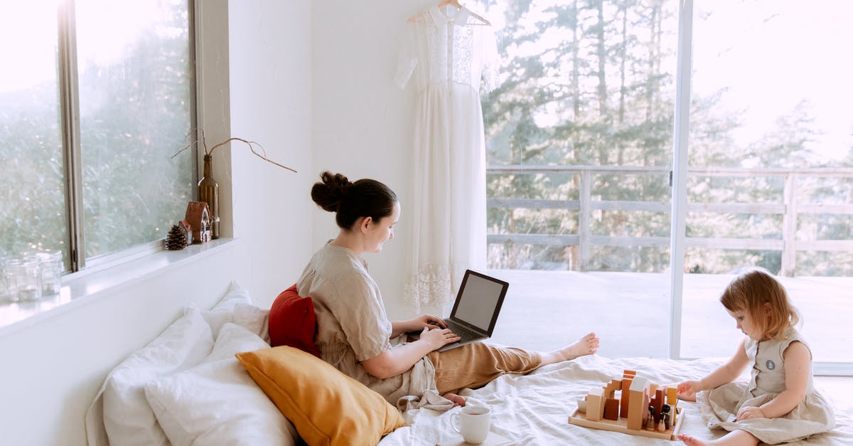 How do I use game tickets? - Side view of cute toddler girl sitting on bed barefoot and playing with colorful wooden blocks while mother using laptop in bed enjoying morning coffee