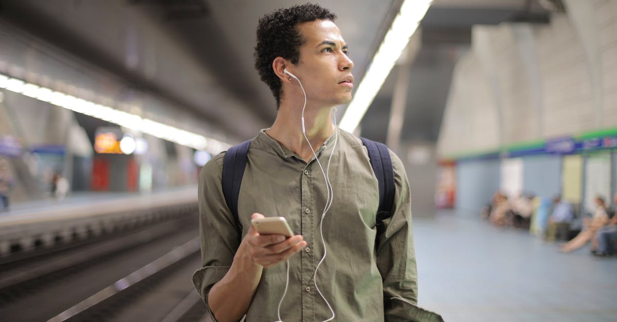 How do the underground statues actually work? - Young ethnic man in earbuds listening to music while waiting for transport at contemporary subway station