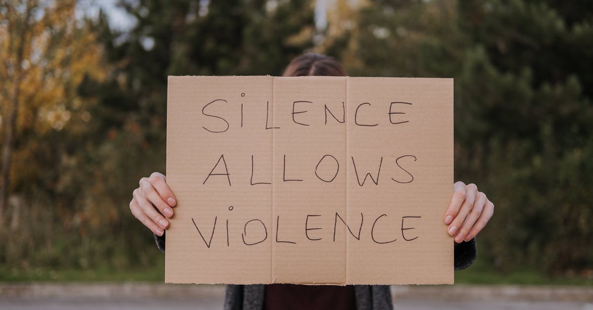 How do you change control schemes? - Anonymous person showing slogan silence allows violence on cardboard on road near green trees