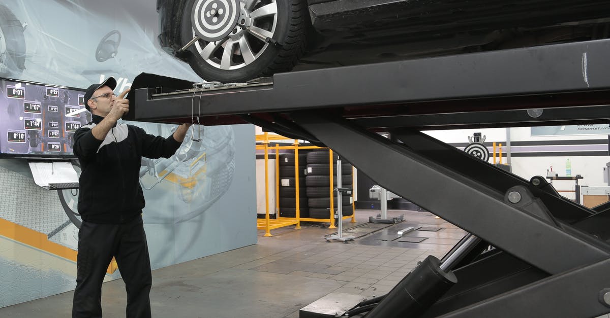 How do you operate the elevator in Stellar Bay? - Serious mechanic checking car wheels on lift in modern car service garage