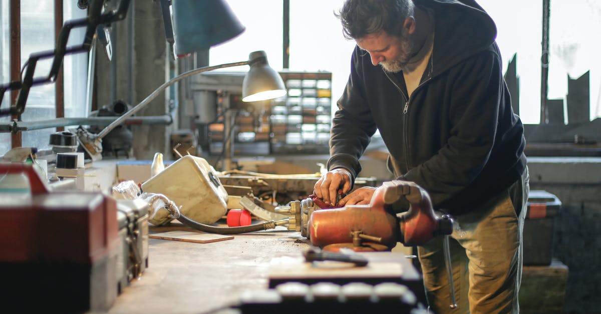 How does Hextech Crafting work? - Side view of serious middle aged male in workwear standing near workbench and working with tools and metal details in lamplight in workshop