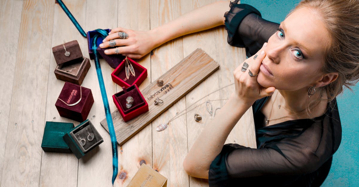 How does Mom's Box work with swallowed trinkets? - From above serious businesswoman looking up at camera while sitting at wooden table with small jewelry boxes with bijouterie and decorating with ribbon as present