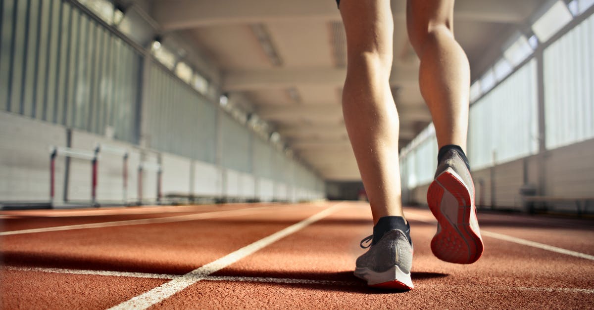 How does the Arena work? - From below back view of crop strong runner walking along running track in athletics arena while doing warm up exercises during workout