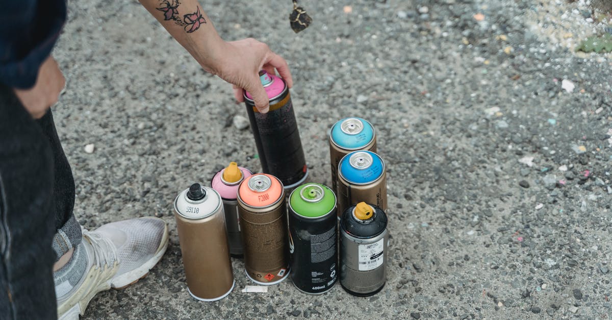 How many bananas can a farmer collect at once? - Crop anonymous person in sneakers with tattoo and heap of multicolored spray paint cans on ground standing on street in city