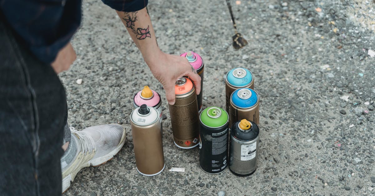 How many bananas can a farmer collect at once? - Crop faceless tattooed artist taking paint bottle from heap of multicolored spray cans placed on ground on street of city