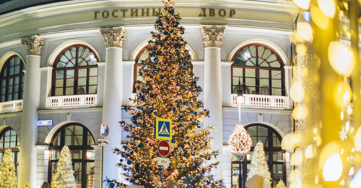 How to beat Giant Cactuar (mission 54) with 5 stars? - Low angle of decorated Christmas tree with blue and golden toys and glowing lamps on street against exterior of old building in evening city