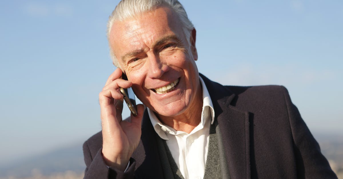 How to chat to all - Delighted male entrepreneur wearing classy jacket standing in city and making phone call while smiling and looking at camera