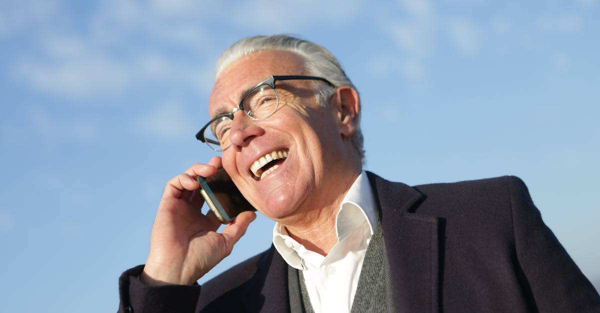 How to chat to all - From below of delighted aged male entrepreneur in classy outfit standing on street and speaking on cellphone while laughing and looking away