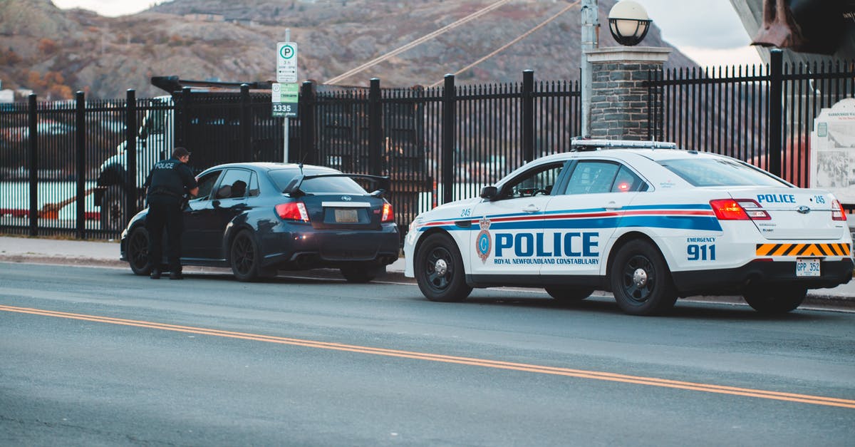 How to check laws of other kingdoms? - Back view of unrecognizable police officer in uniform checking modern car parked on asphalt road against cloudy sky