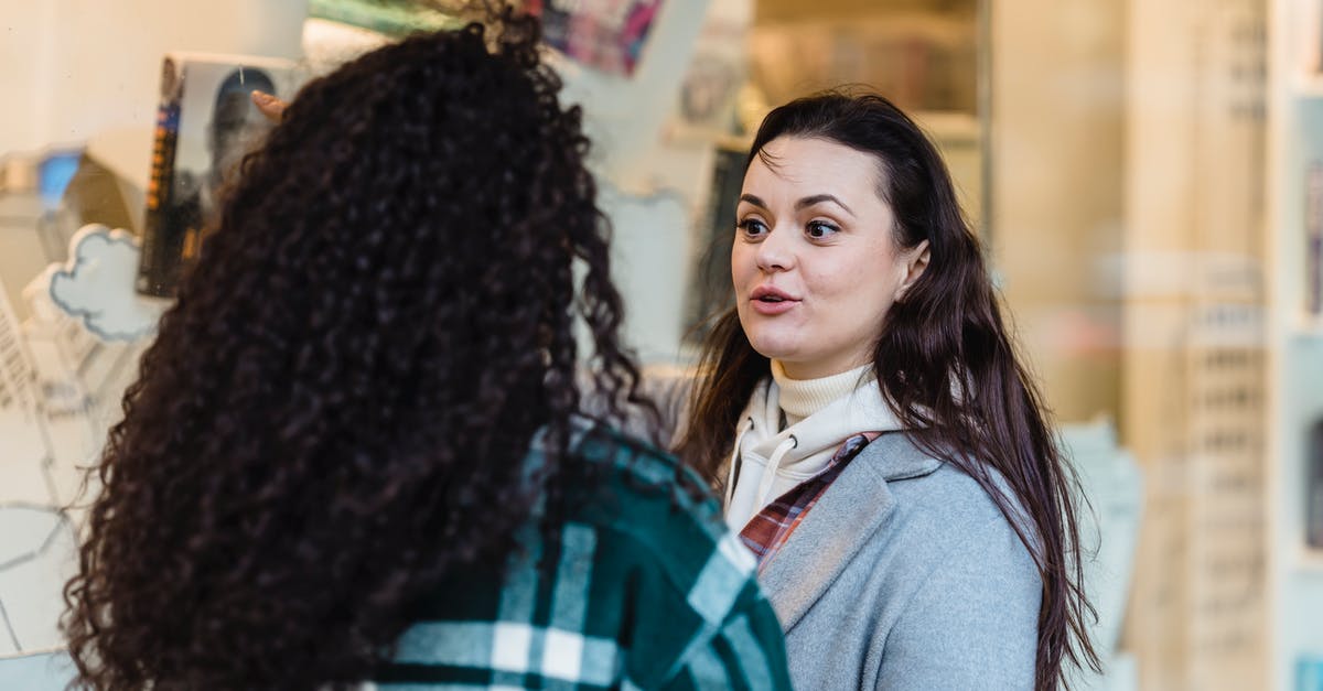 How to choose dialogue options via keyboard? - Positive woman communicating with unrecognizable female friend while standing near glass shop window of store with souvenirs on street in city