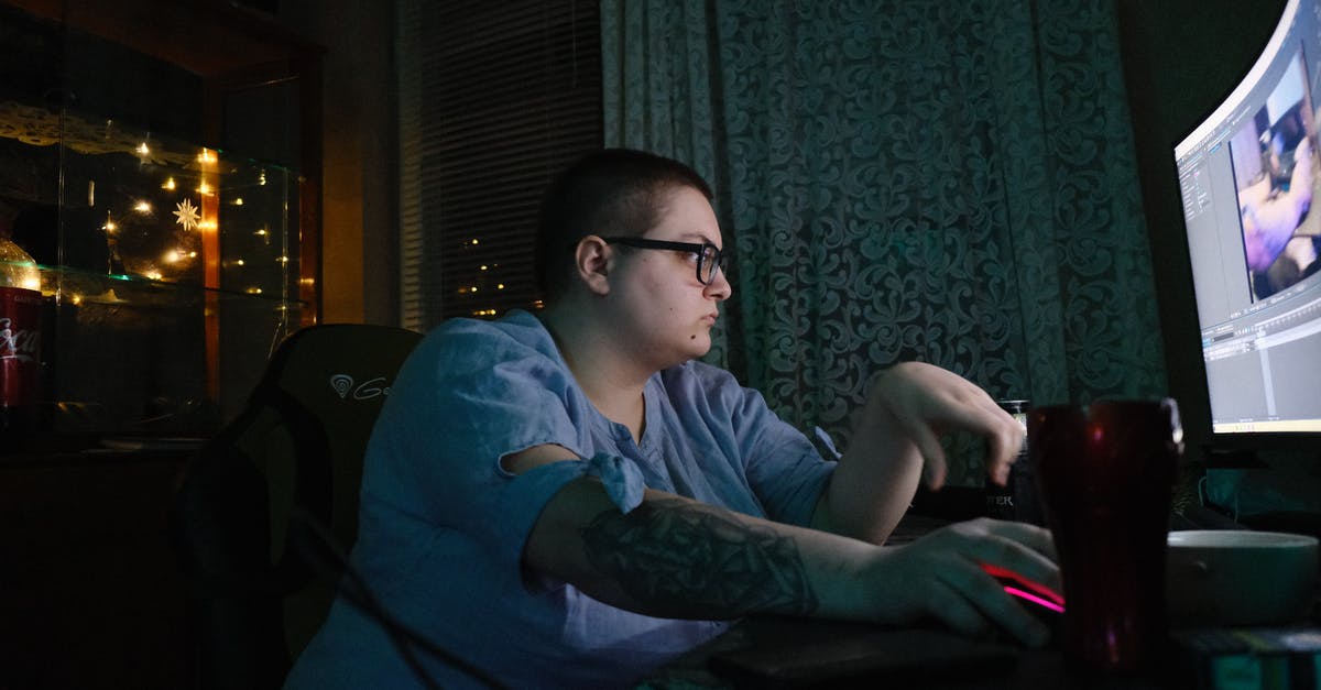 How to deinterlace SNES video for PC play/capture? - Side view of obese young male in eyeglasses with tattooed arm sitting at table and using computer with curved monitor while spending evening at home