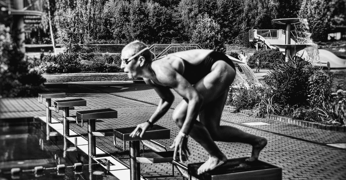 How to fill a block with an Armor Stand - Black and white side view full body sporty swimmer in swimming suit and goggles standing on block in track start position preparing to dive in outside pool