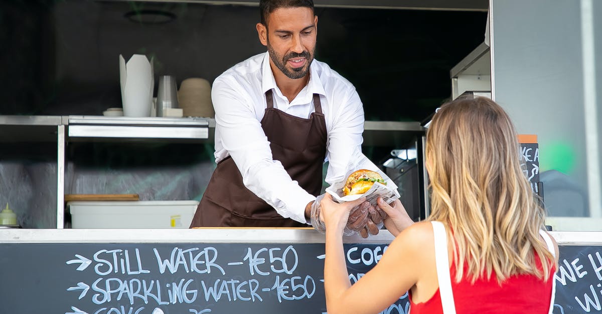 How to give vassals provinces? - Positive ethnic cook in apron standing at counter in food truck and giving delicious hamburger to anonymous woman customer in daytime