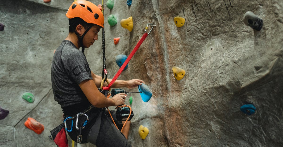 How to improve at low 6 digit rank (~200-100k)? - From below of side view of Asian male specialist in helmet drilling hole in blue climbing hold while hanging on safety rope near bouldering wall