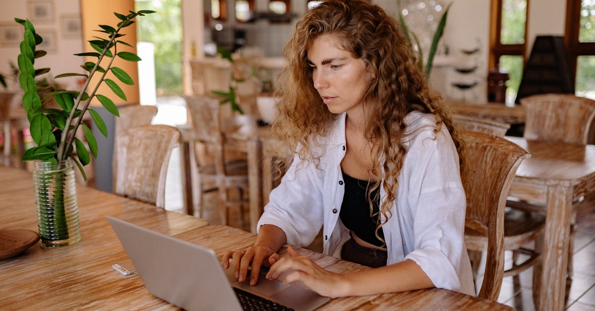 How to make a lingering potion stay longer? - Content female customer with long curly hair wearing casual outfit sitting at wooden table with netbook in classic interior restaurant while making online order