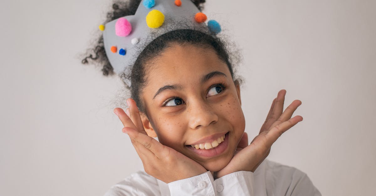 How to make Oleana appear in Crown Tundra? - Happy African American girl with curly hair and gray crown with colorful pompoms smiling and looking away with hands at chin on white background