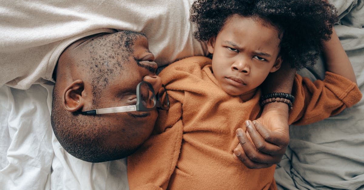 How to unlock the extra content playing by yourself - Top view of African American man in glasses lying near angry child in casual clothes while cuddling together in comfortable bedroom