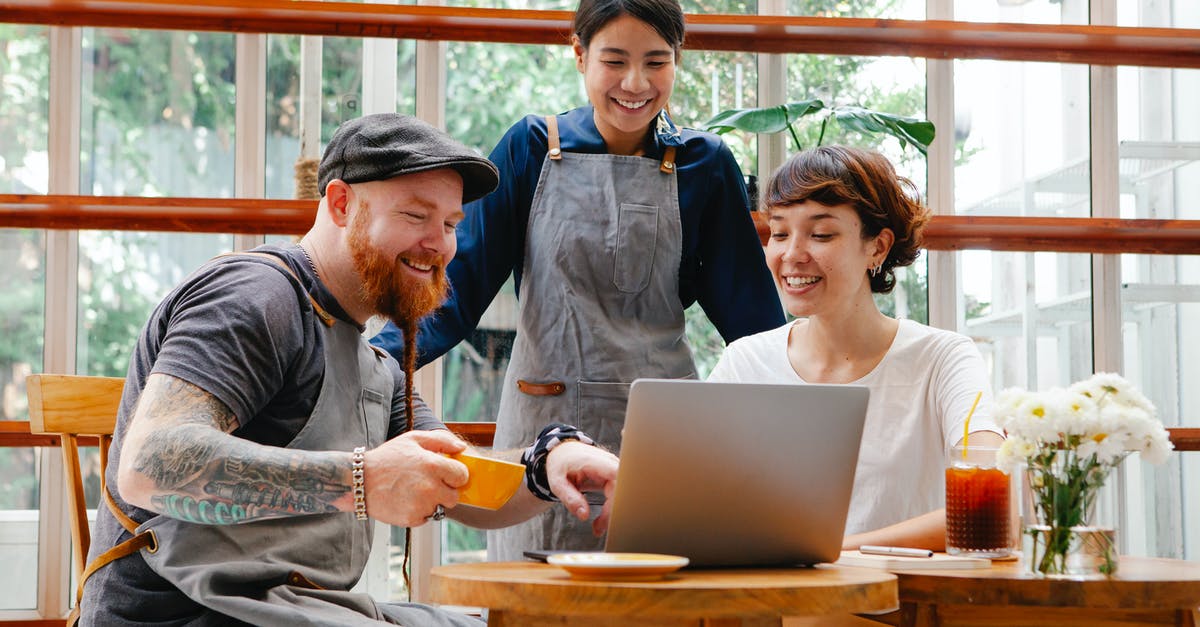 How to use multiple mics while streaming on twitch local - Positive coworkers in aprons and casual outfit using computer in cafeteria at table with coffee cup and glass of drink in day