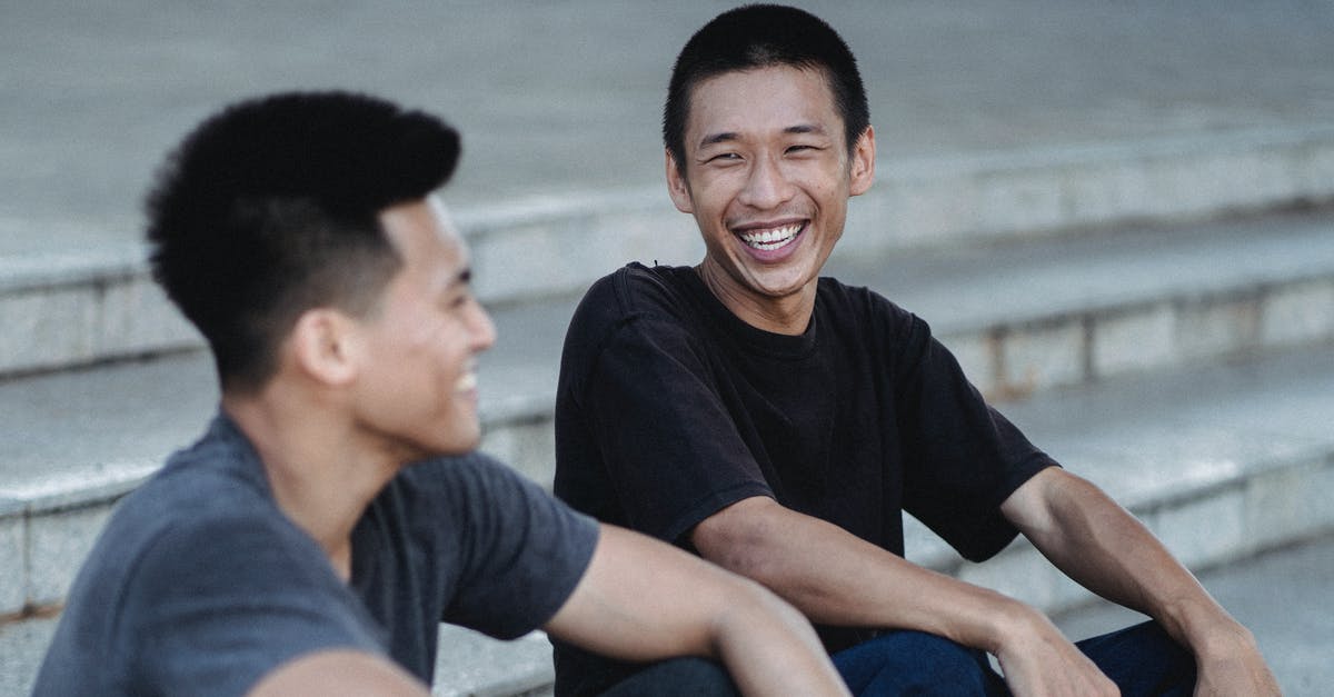 Is it possible to connect PSP Street to TV? - Cheerful Asian male friends in casual wear with dark hair smiling while sitting on stone stairs on street in city