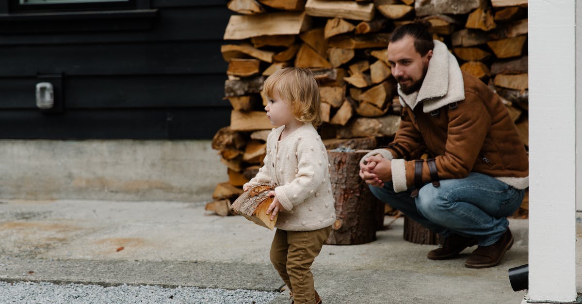 Is it possible to have a strong scout? - Cheerful man smiling while sitting and looking at child while playing with firewood in yard and having fun together during weekend