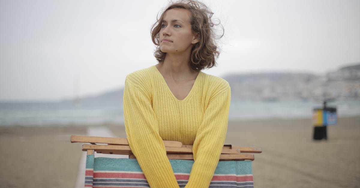 Is it possible to miss the ending scene? - Calm female tourist with folded deckchair standing alone on seashore in overcast weather