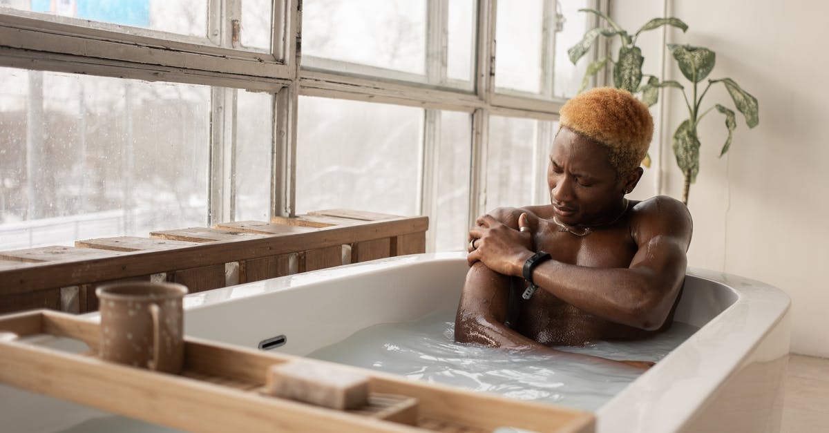 Is it possible to take the badges out to look at them? - Young African American man with dyed hair and accessory sitting in bathtub full of water in light room with shabby window frames